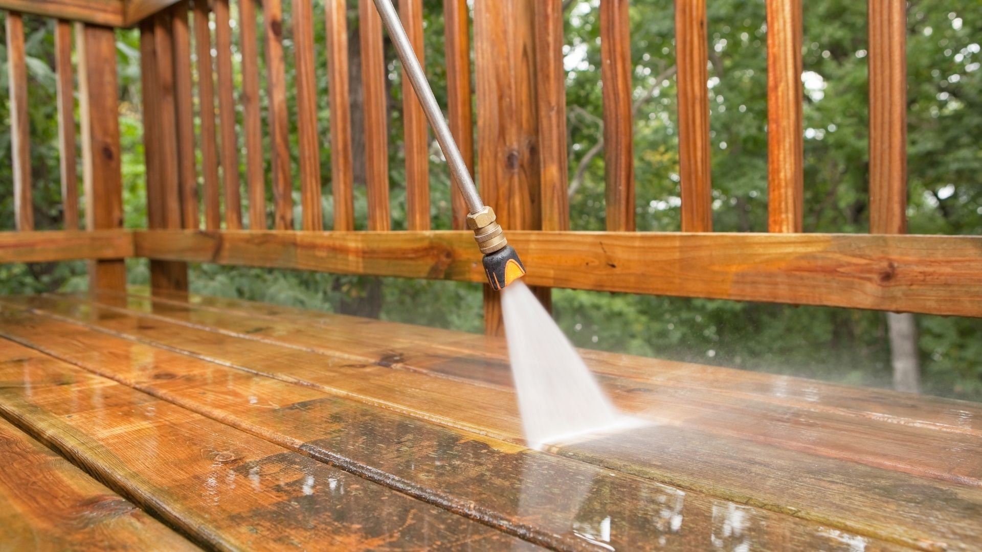 Pressure washer cleaning wooden deck with water spray and stream