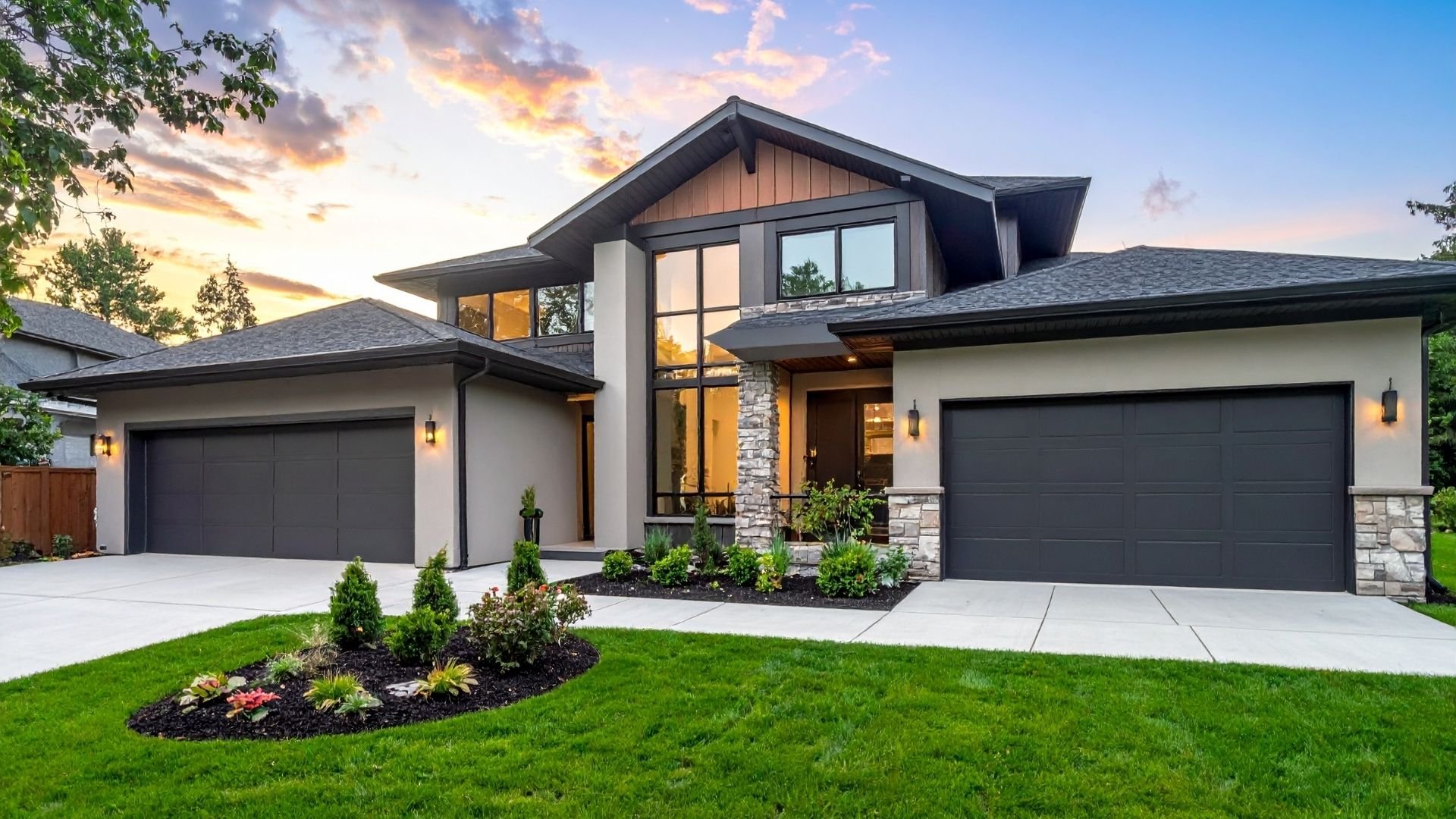 Modern two-story home with black garage doors, stone accents, and landscaped yard at sunset.