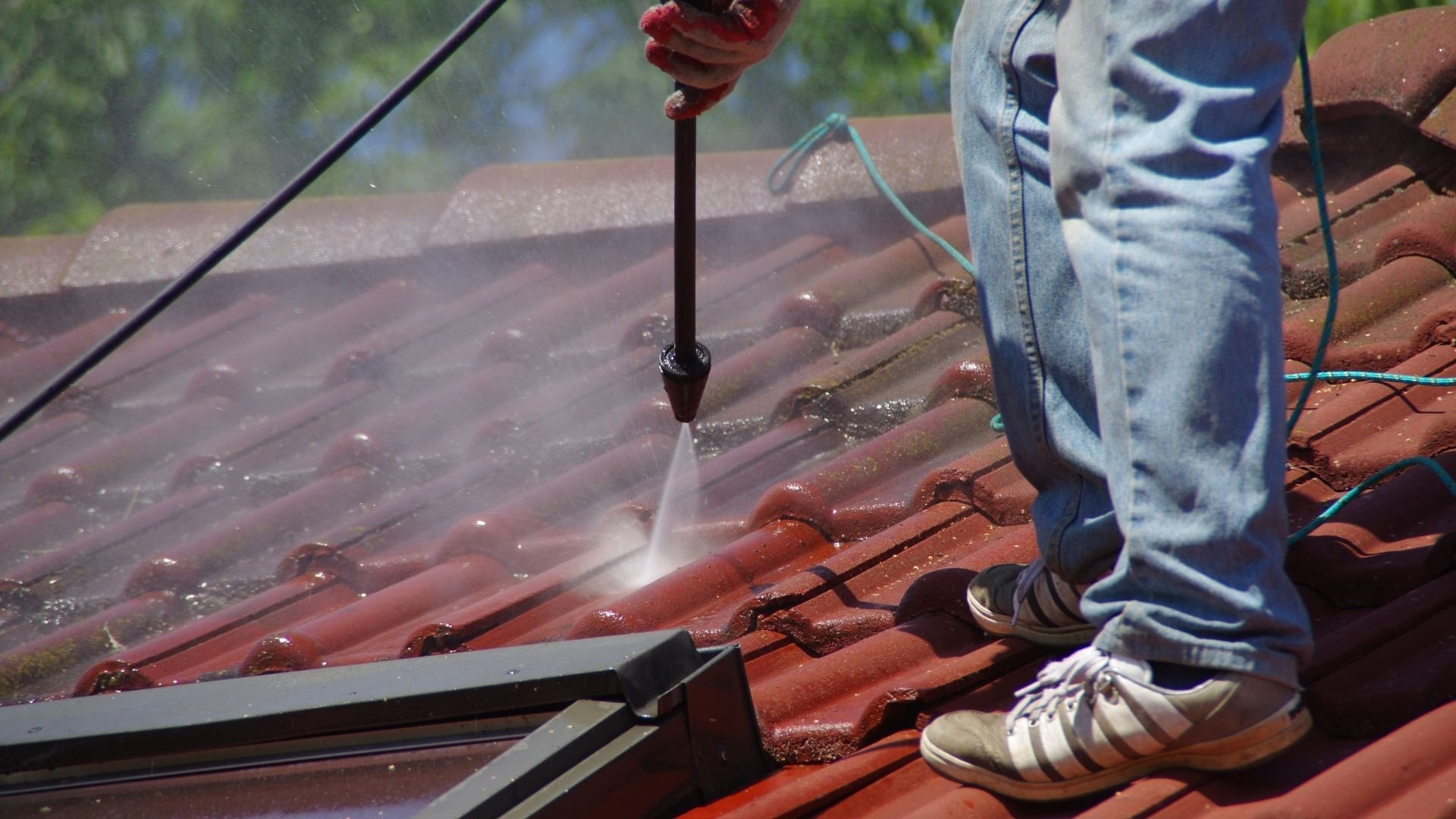 Person pressure washing red roof tiles with water spray, wearing sneakers.