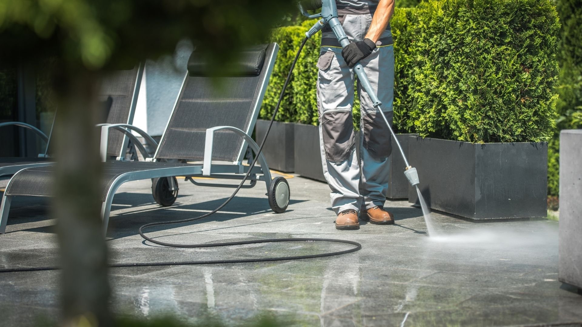 Worker power washing a patio floor with pressure washer equipment and hose