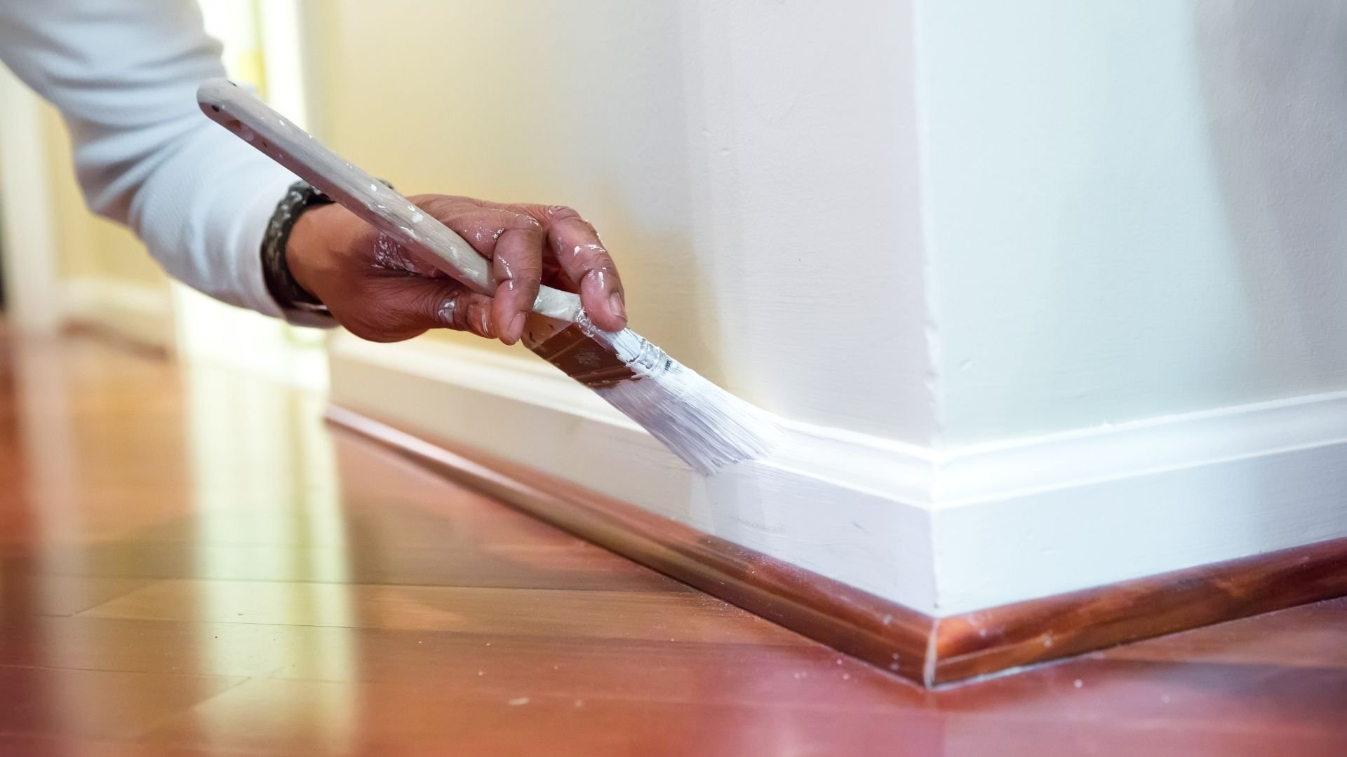 Person painting white trim with a brush on wooden frame indoors.