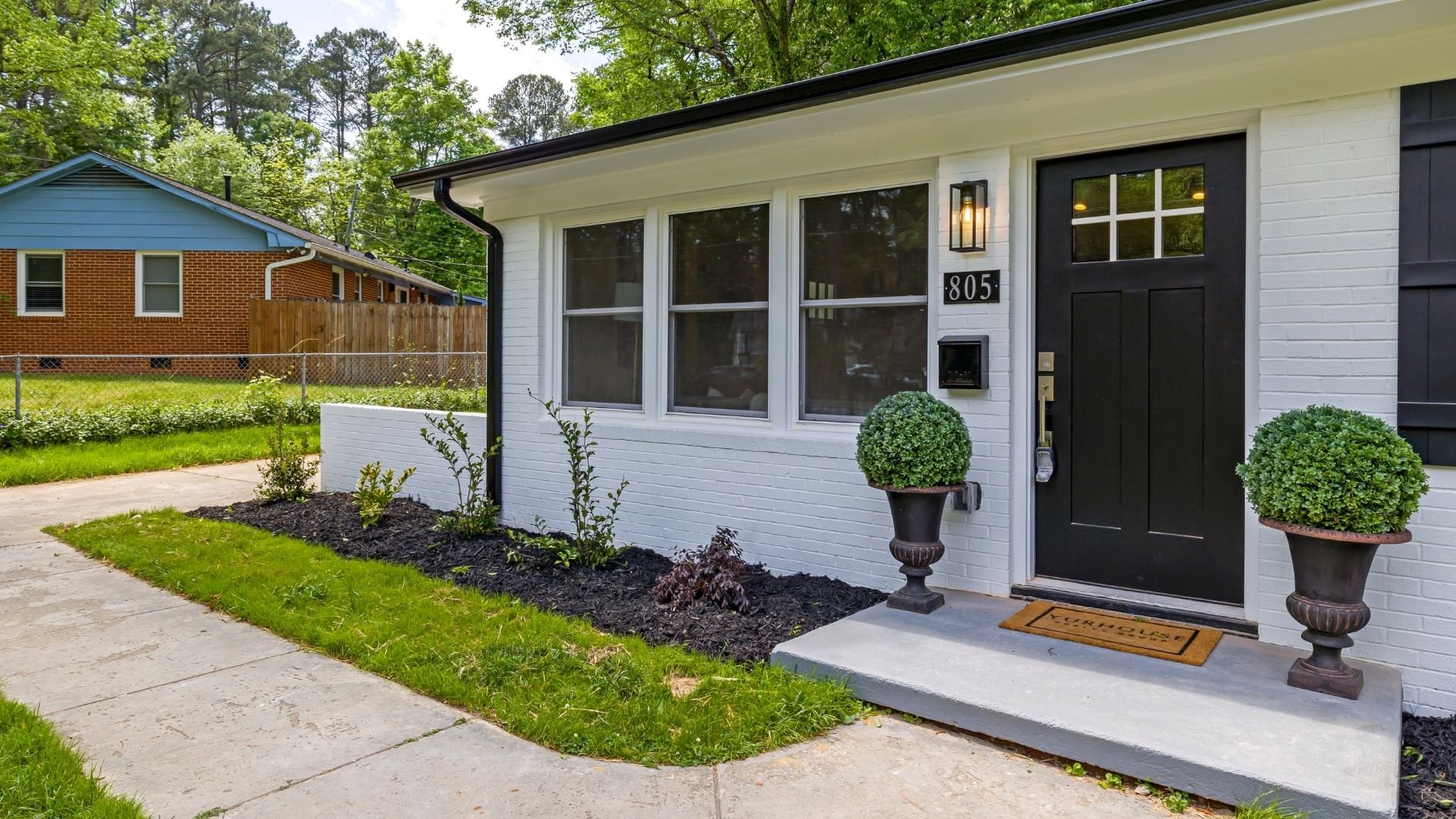 Modern white house exterior with black door, landscaped front yard, and potted topiaries.